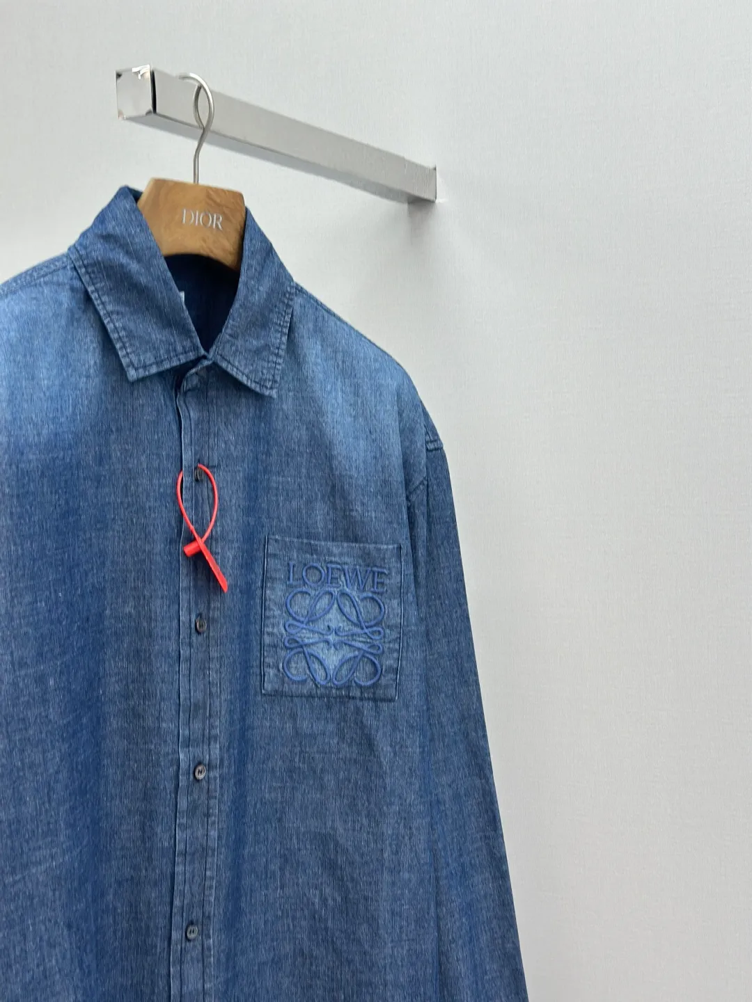 P430 Loewe Anagram Gradient Embroidered Pocket Shirt Made of custom-made high-quality cotton chambray fabric, with a unique washed gradient blue as the main tone, from dark to light and from thick to light. The chest patch pocket is decorated with Loewe Anagram embroidery as its soul, engraved with LOEWE-style casual elegance, and the natural and smooth lines show the casualness.  Imported embroidery machines are used, and advanced computer control systems and precision mechanical components are used to realize Loewe embroidery operations.  The gradient dynamic spray dyeing process uses specialized spray dyeing equipment to accurately spray dye onto the surface of the fabric in the form of mist (by accurately controlling the different dimensions of the spray of the spray dyeing equipment, combined with the movement speed and direction during the dyeing process) to present a smooth and natural transition effect of color. The butterfly rhyme pinch pleating body dart technology is inspired by the beautiful shape of butterflies, and uses precise pinch pleating techniques to create a flexible pleat effect like butterfly wings on the garment, making the garment fit more closely to the body.  size:44.46.48.50